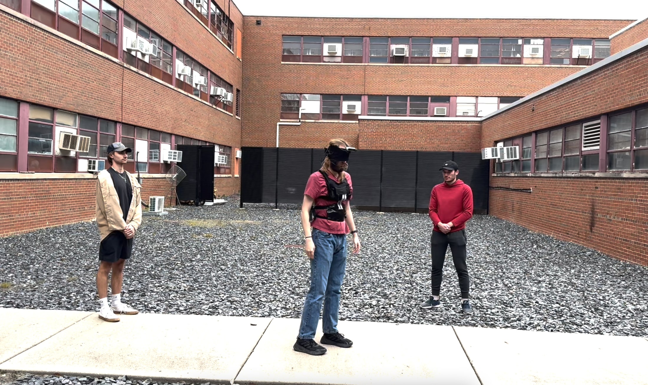 Blindfolded tester crossing a courtyard using the wearable system while two teammates observe